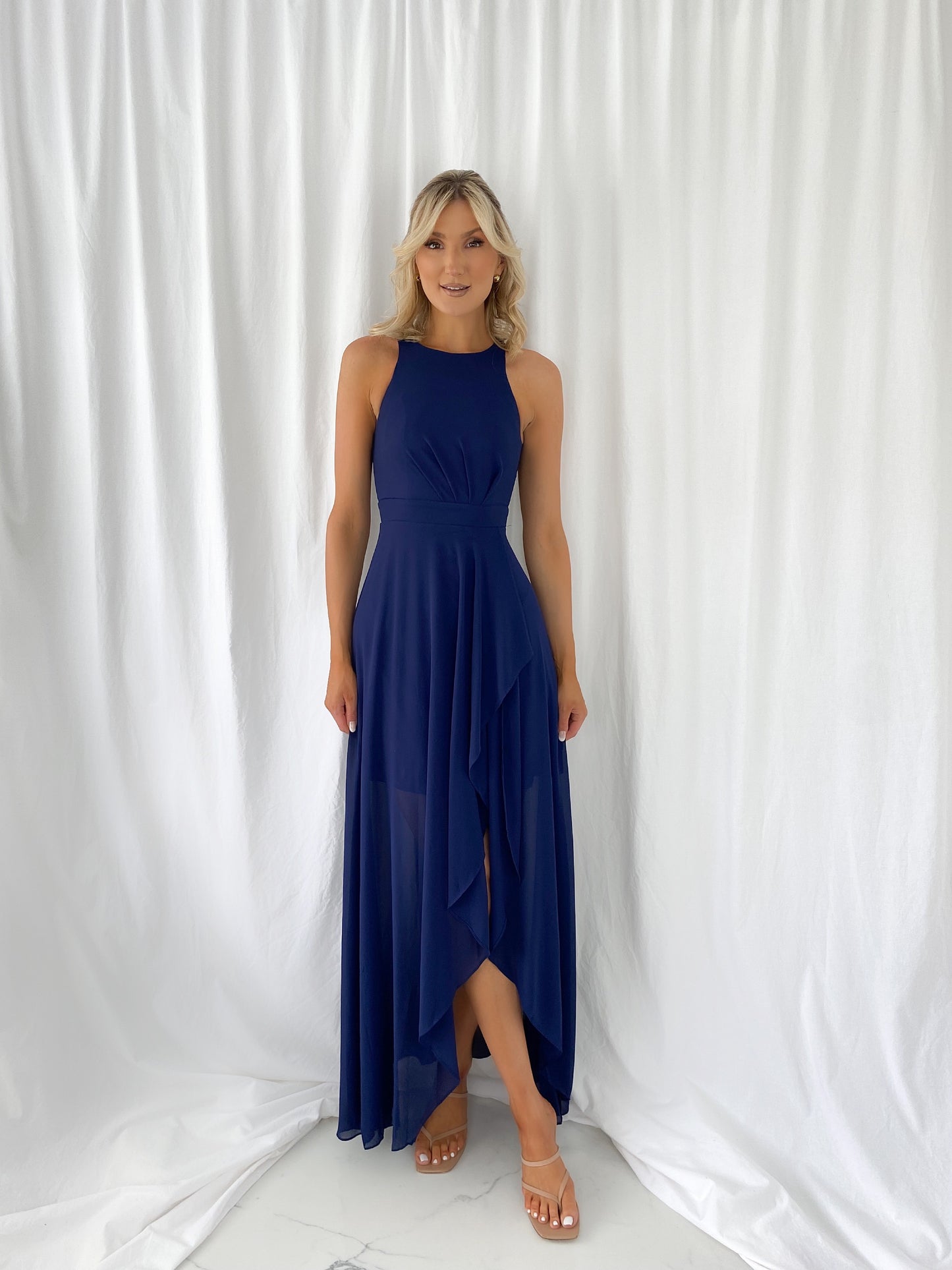 a woman in a blue dress standing next to a white curtain