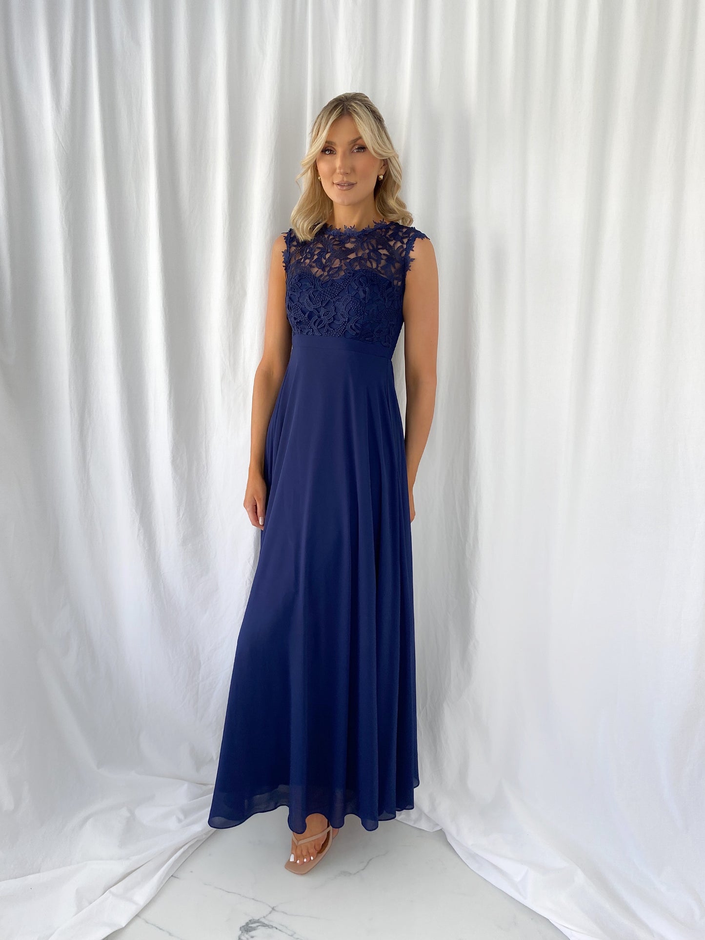 a woman in a blue dress standing next to a white curtain