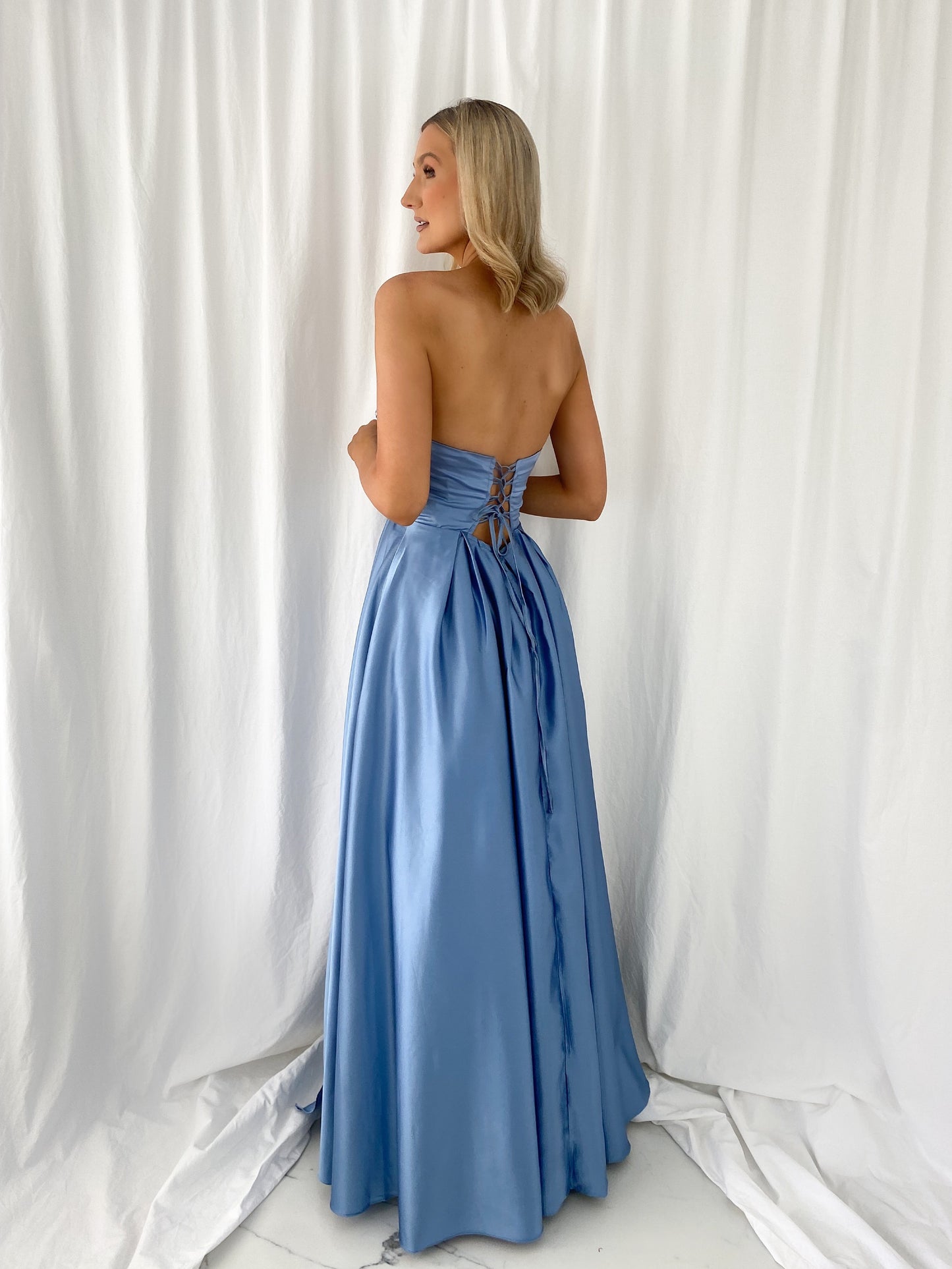 a woman in a white dress is holding a blue suitcase