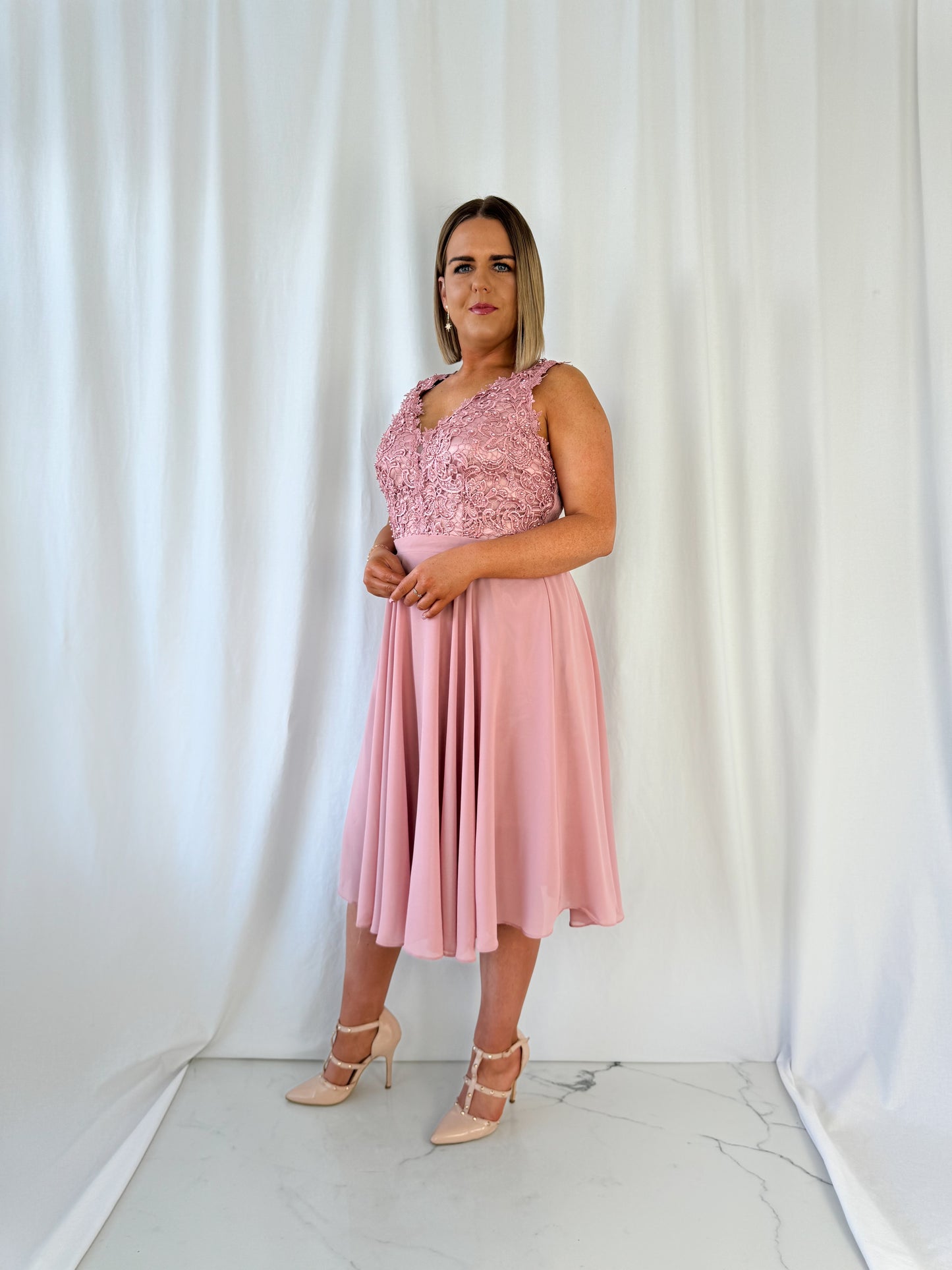 a woman in a pink dress standing in front of a curtain 