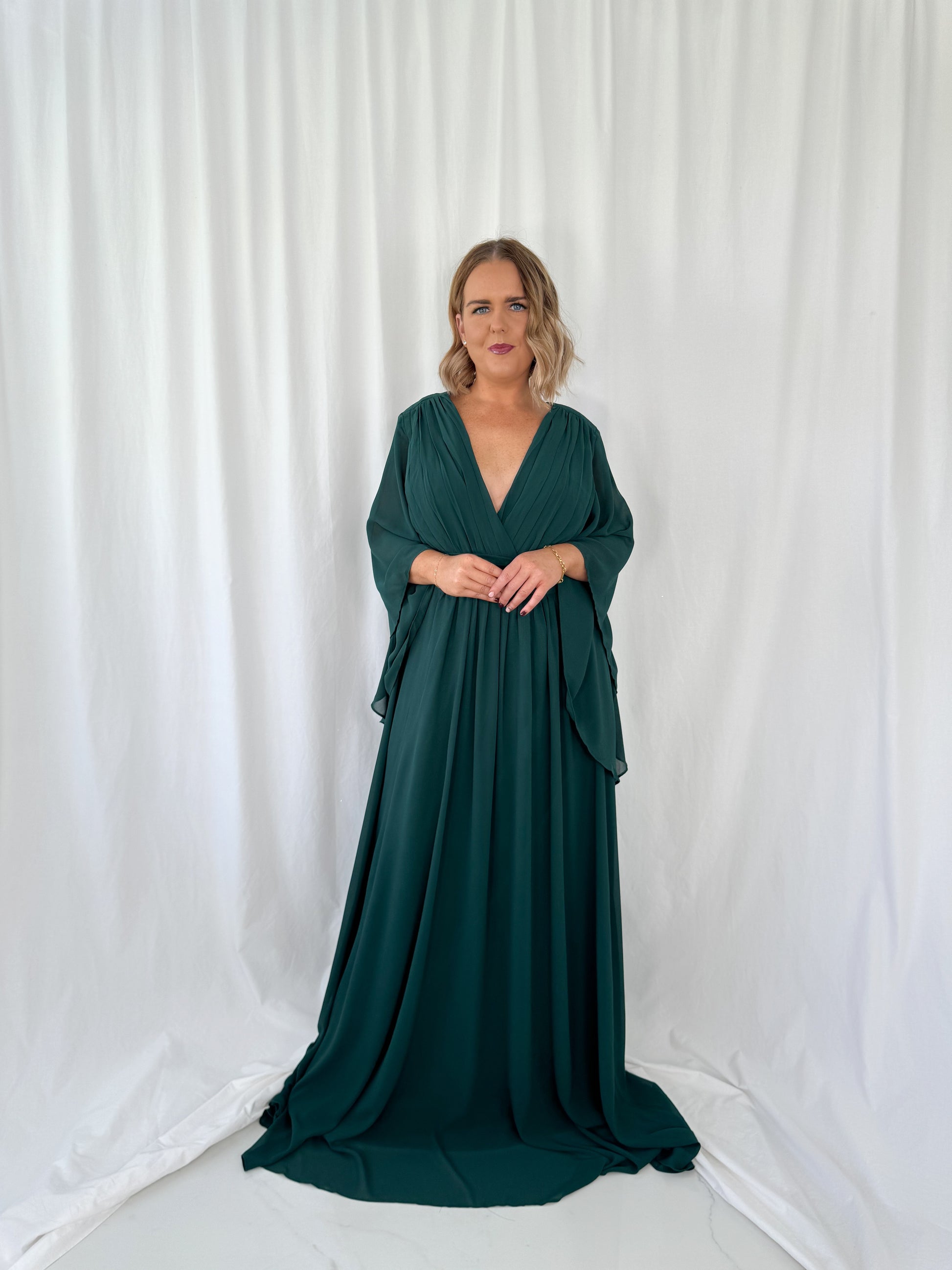 a woman in a green dress standing in front of a curtain 