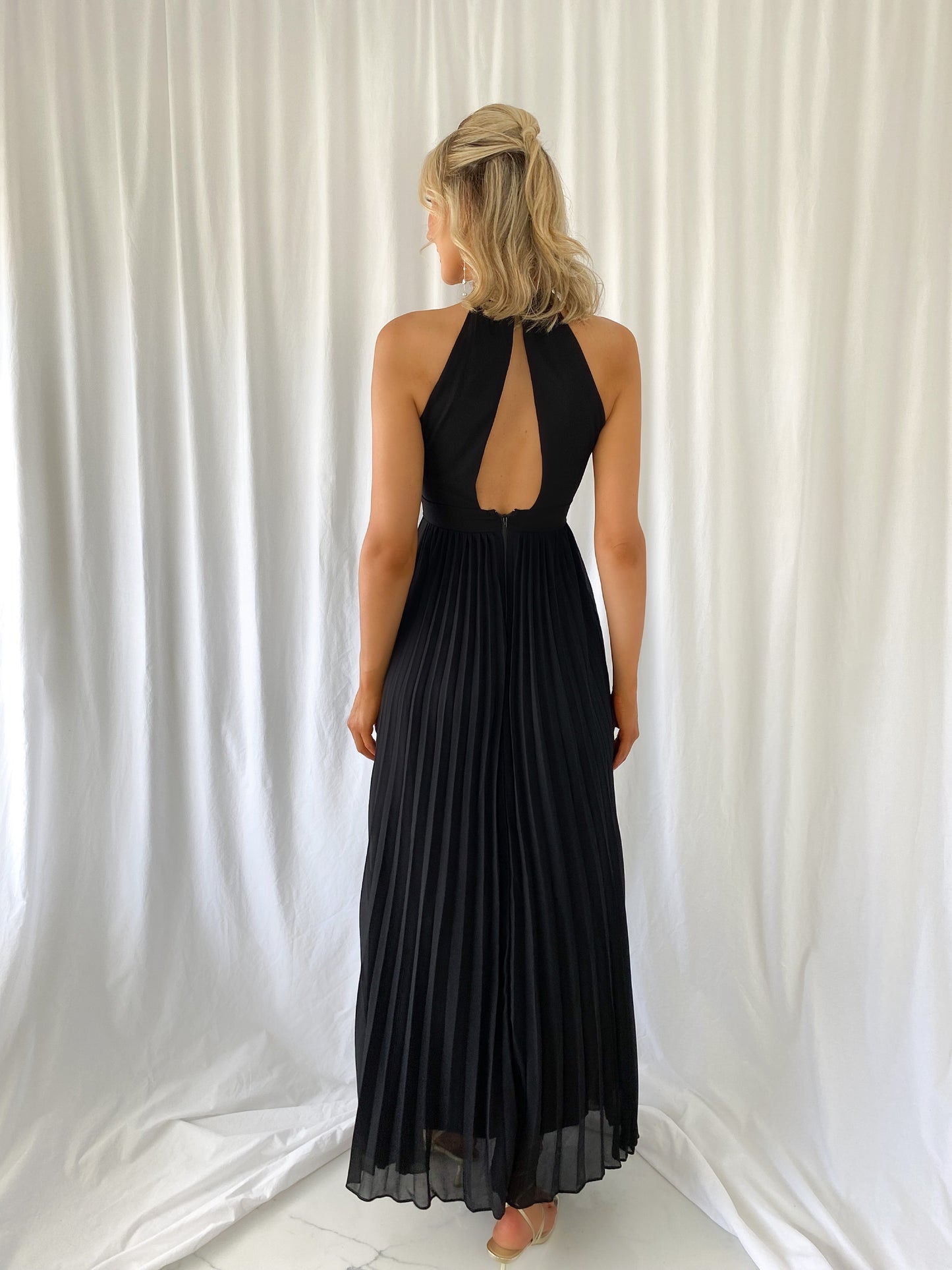 a woman in a black dress standing in front of a curtain 