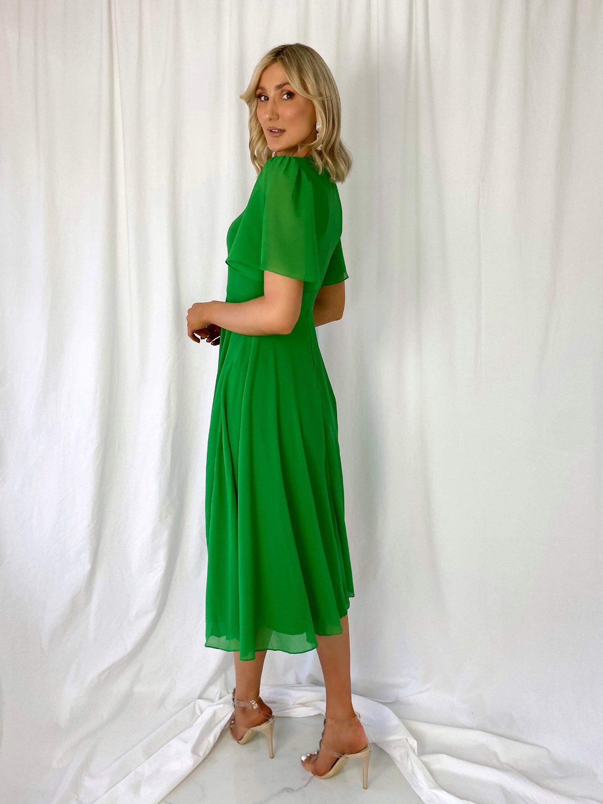 a woman in a green dress standing in front of a wall 